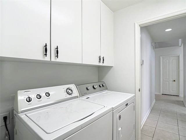 clothes washing area with independent washer and dryer, light tile patterned floors, baseboards, and cabinet space