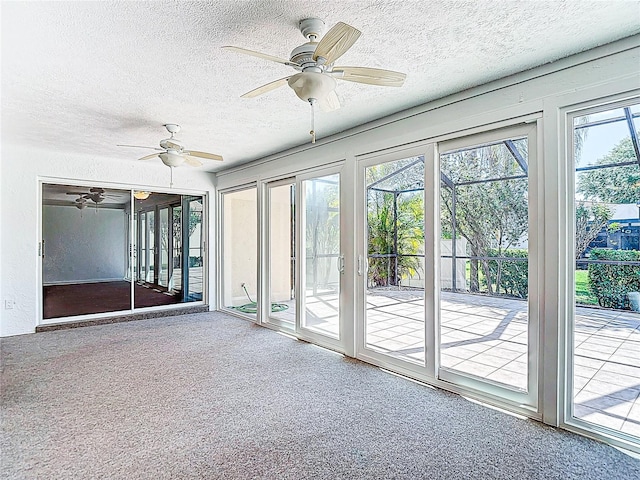 unfurnished sunroom featuring ceiling fan, a textured ceiling, and carpet floors