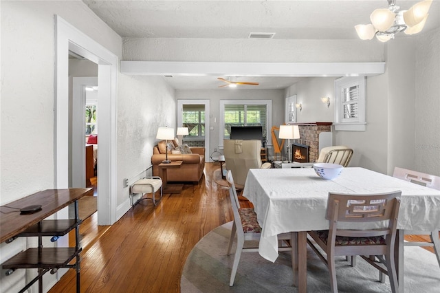 3120 8th Ave N, Saint Petersburg, FL 33713 - dining area with hardwood / wood-style flooring, a fireplace, a chandelier, a textured wall, and beamed ceiling