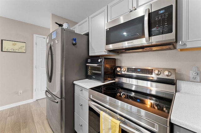 kitchen with appliances with stainless steel finishes, light wood-style flooring, and baseboards