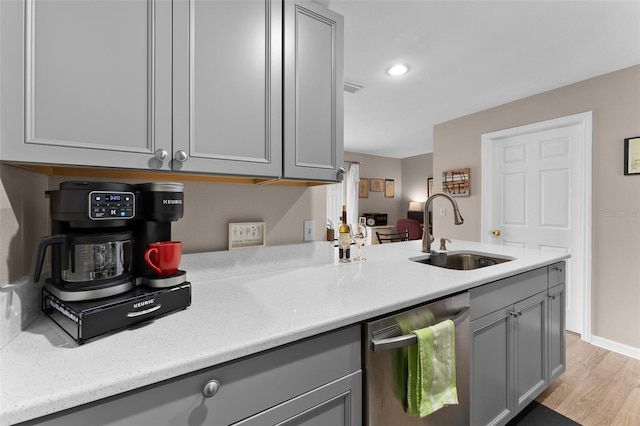 kitchen with a sink, dishwasher, gray cabinets, light wood-style flooring, and light stone counters