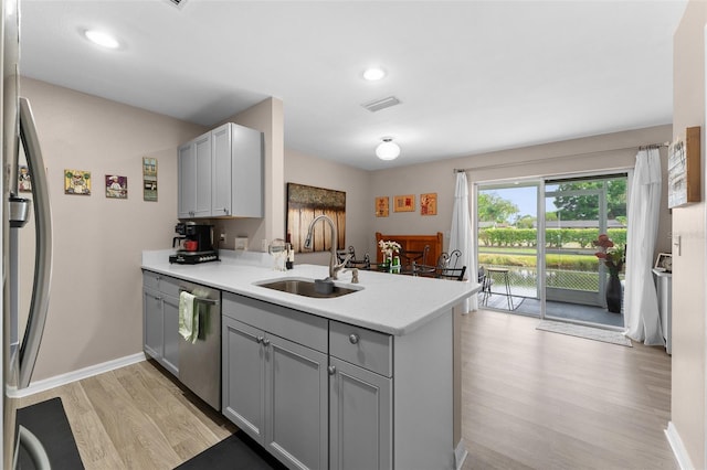 kitchen with a sink, gray cabinetry, appliances with stainless steel finishes, light wood-style floors, and a peninsula