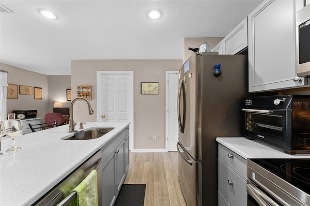 kitchen with a sink, light countertops, appliances with stainless steel finishes, light wood finished floors, and recessed lighting