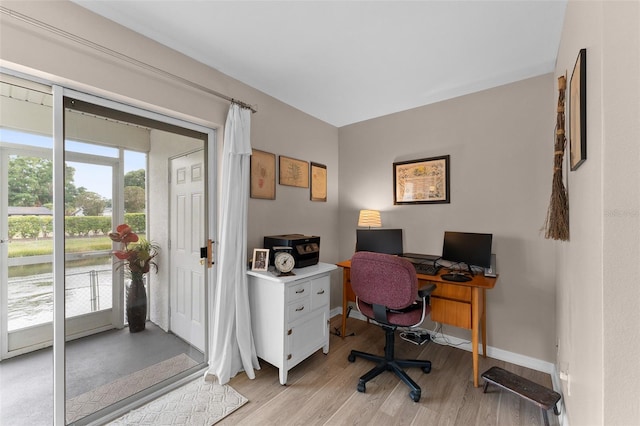 home office with light wood finished floors, baseboards, and a water view