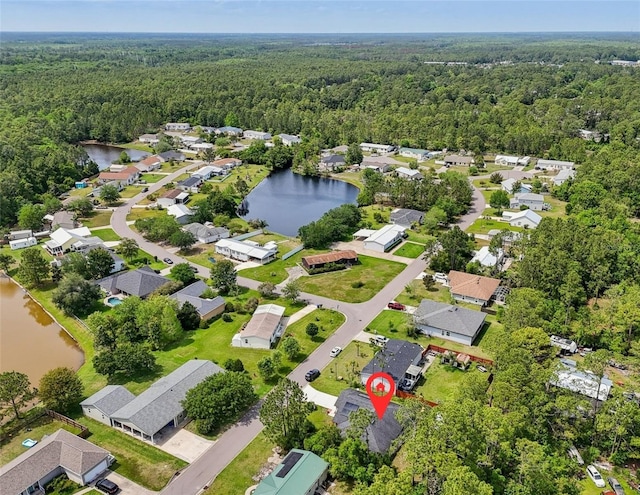 aerial view of property and surrounding area featuring a heavily wooded area, a nearby body of water, and nearby suburban area