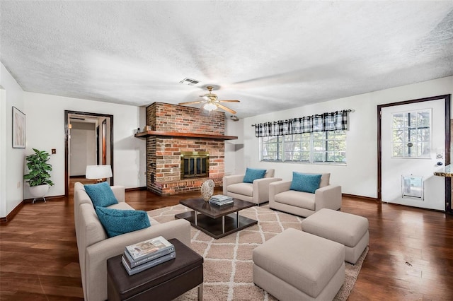 living room with visible vents, a brick fireplace, a ceiling fan, a textured ceiling, and wood finished floors