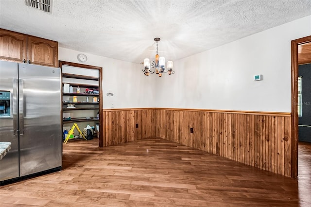 unfurnished dining area with a chandelier, visible vents, light wood finished floors, and wainscoting