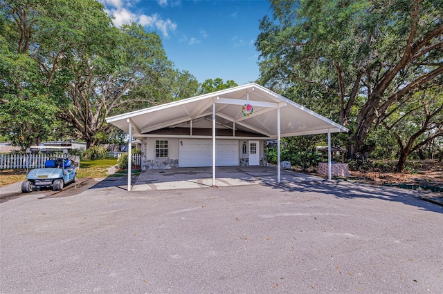 view of parking with a carport, an attached garage, fence, and aphalt driveway