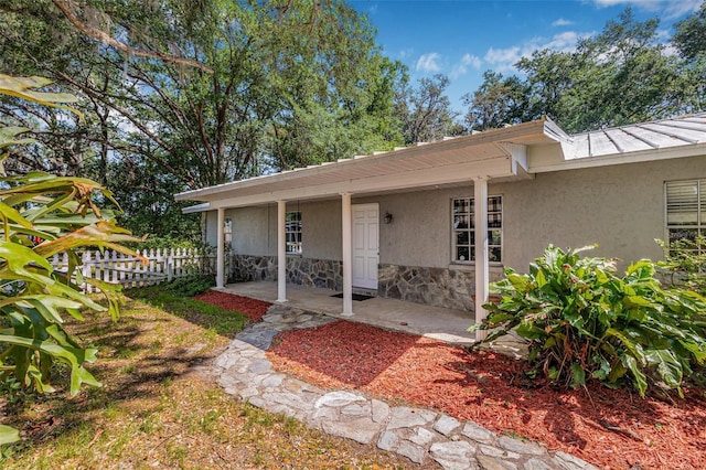 property entrance featuring a patio, stucco siding, stone siding, and fence