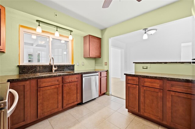 kitchen featuring ceiling fan, stainless steel dishwasher, a sink, dark stone countertops, and light tile patterned flooring