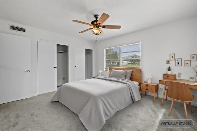 carpeted bedroom featuring visible vents, multiple closets, and ceiling fan