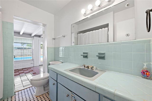 full bathroom featuring vanity, toilet, a wainscoted wall, tile walls, and beamed ceiling