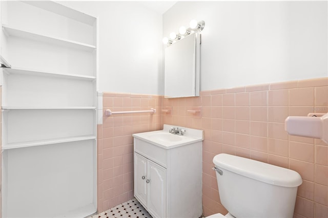 bathroom with toilet, tile walls, wainscoting, and vanity