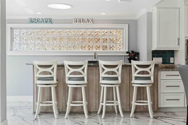 interior space with white cabinets, crown molding, marble finish floor, decorative backsplash, and a kitchen bar