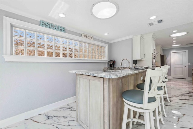 kitchen with a breakfast bar area, visible vents, baseboards, marble finish floor, and oven