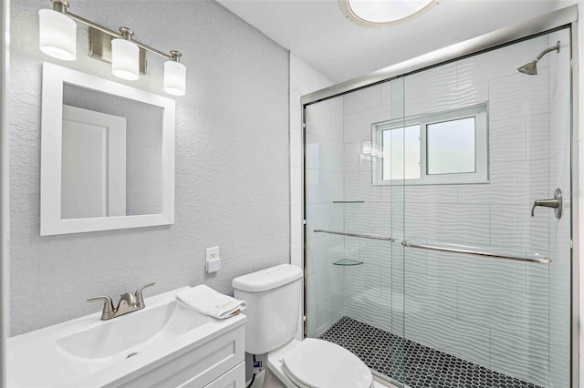 bathroom with toilet, a textured wall, a shower stall, and vanity