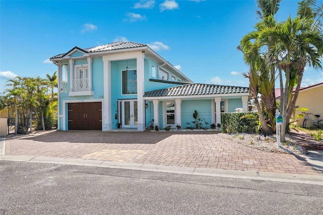 view of front facade featuring a garage, a balcony, stucco siding, french doors, and a tiled roof