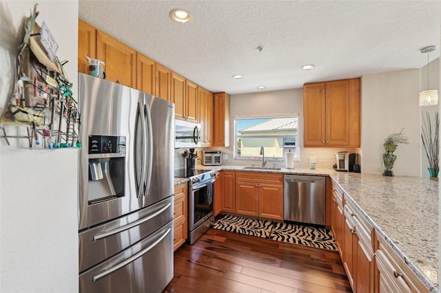 kitchen with decorative backsplash, a sink, appliances with stainless steel finishes, dark wood-style floors, and light stone countertops
