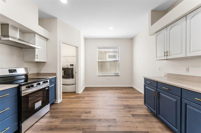 kitchen featuring stainless steel electric range oven, blue cabinetry, white cabinets, washer / dryer, and wall chimney exhaust hood