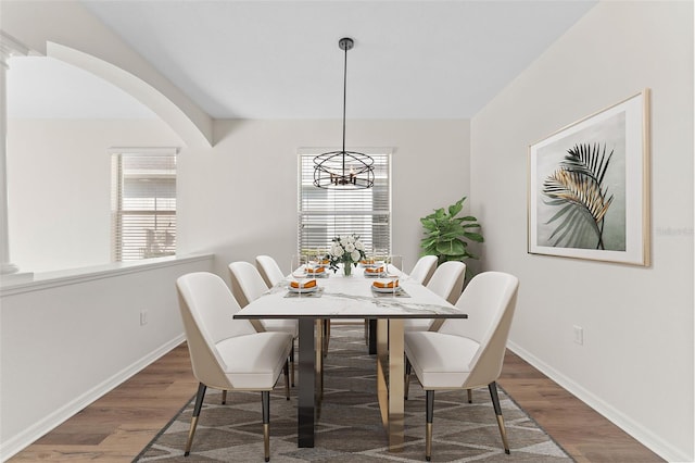 dining space with a chandelier, arched walkways, baseboards, and wood finished floors