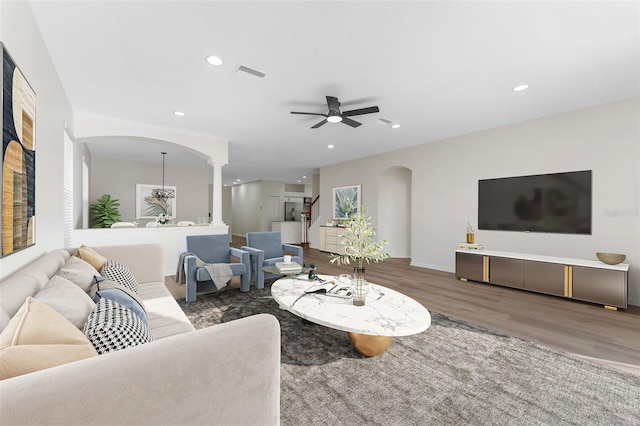 living room featuring visible vents, ceiling fan, decorative columns, arched walkways, and wood finished floors