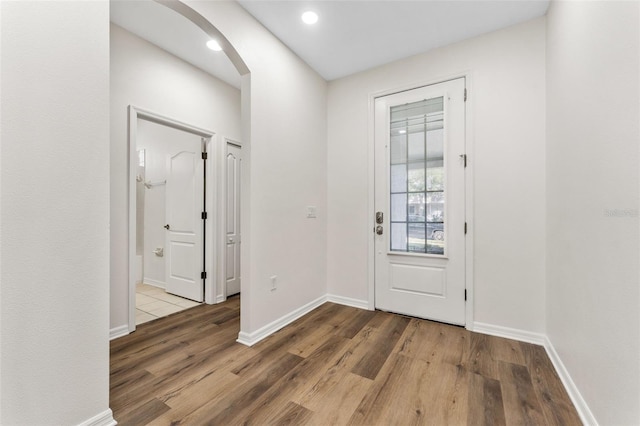 entryway featuring arched walkways, wood finished floors, and baseboards