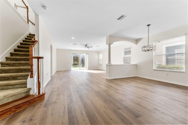 unfurnished living room with visible vents, baseboards, arched walkways, wood finished floors, and stairs