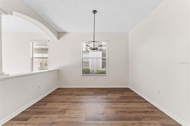unfurnished dining area with baseboards, plenty of natural light, a chandelier, and wood finished floors