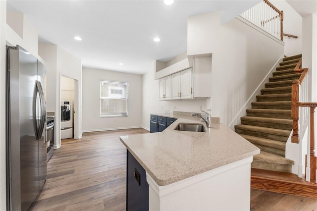 kitchen with freestanding refrigerator, a peninsula, washing machine and clothes dryer, a sink, and light wood finished floors