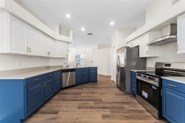 kitchen with wall chimney exhaust hood, a peninsula, white cabinetry, stainless steel appliances, and blue cabinets