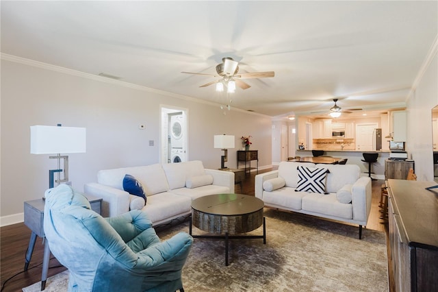 living area with baseboards, a ceiling fan, wood finished floors, stacked washing maching and dryer, and ornamental molding