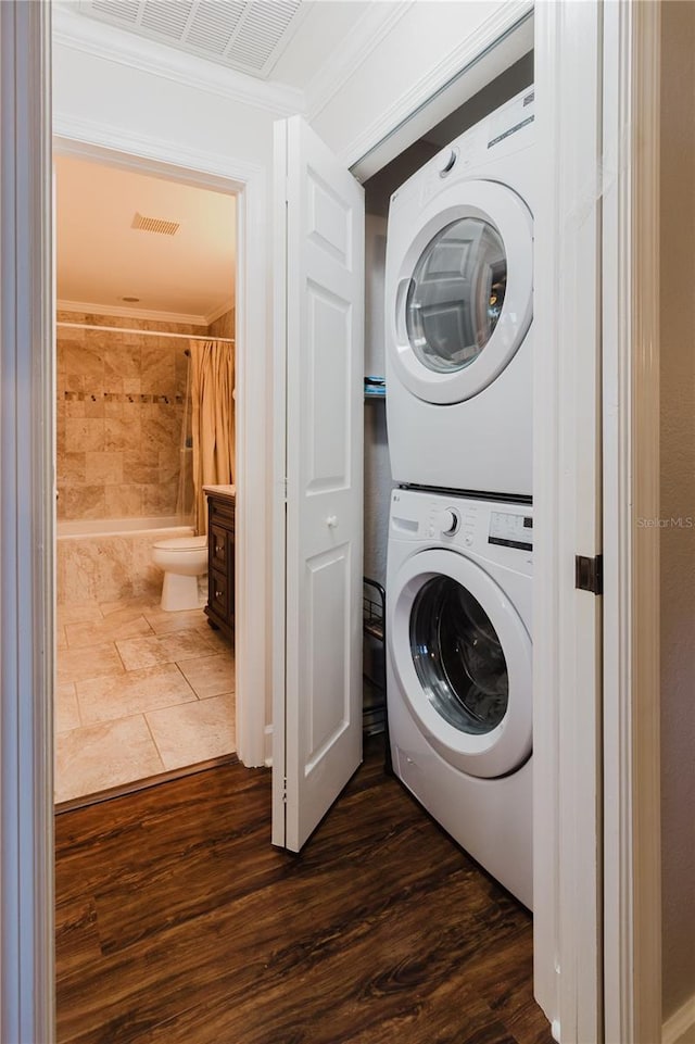laundry area featuring dark wood-style flooring, visible vents, stacked washer and clothes dryer, and laundry area