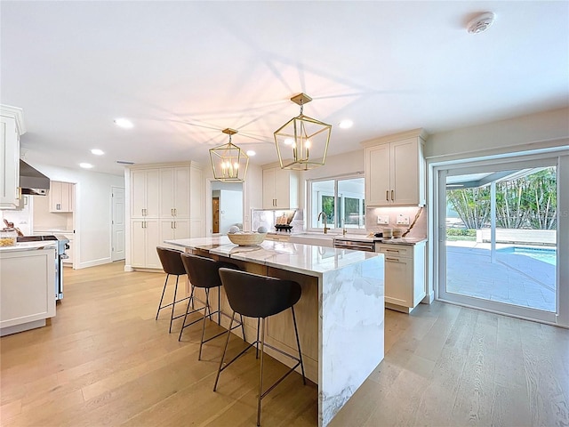 773 Snug Is, Clearwater Beach, FL 33767 - kitchen with wall chimney range hood, light wood-type flooring, a kitchen island, recessed lighting, and light stone countertops