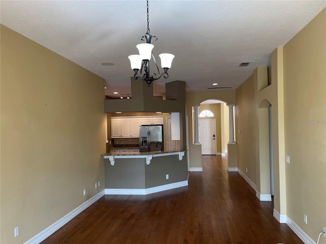 kitchen with arched walkways, dark wood finished floors, stainless steel fridge with ice dispenser, and a peninsula