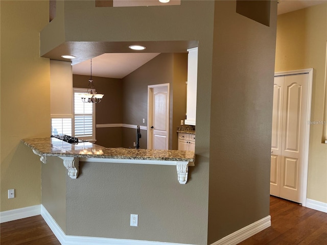 kitchen featuring baseboards, stone countertops, a kitchen bar, and wood finished floors