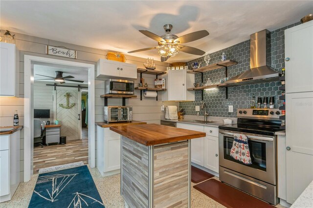 kitchen with a sink, wall chimney range hood, ceiling fan, wood counters, and stainless steel appliances