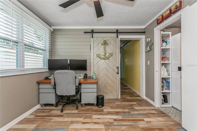 office with baseboards, wooden walls, a barn door, ceiling fan, and wood finished floors