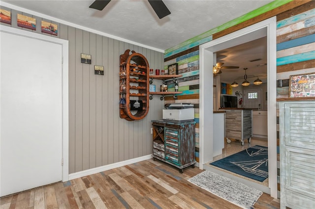 interior space featuring baseboards, ornamental molding, wooden walls, ceiling fan, and wood finished floors