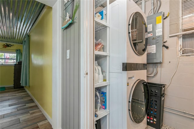 laundry room with laundry area, stacked washer and dryer, water heater, wood finished floors, and baseboards