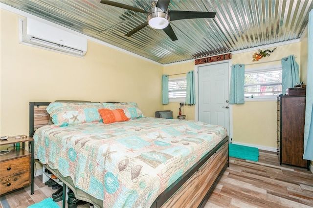 bedroom with a wall unit AC, wood finished floors, and multiple windows