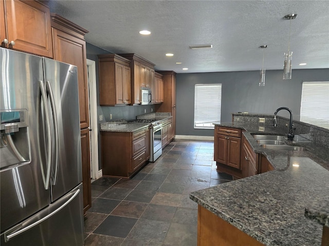 kitchen with a textured ceiling, appliances with stainless steel finishes, a sink, and baseboards