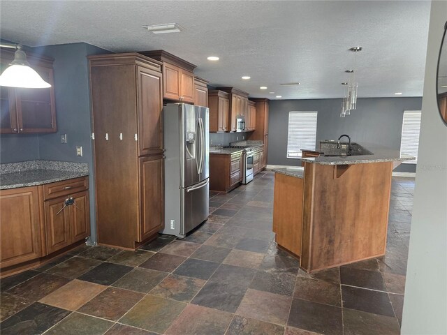 kitchen with stone tile flooring, brown cabinetry, and appliances with stainless steel finishes