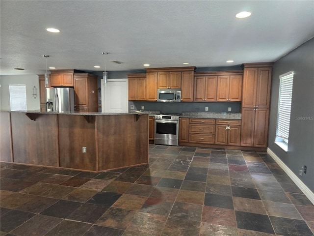kitchen featuring stainless steel appliances, a breakfast bar, brown cabinetry, and a healthy amount of sunlight