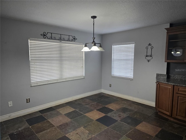 unfurnished dining area with baseboards, stone finish floor, and a textured ceiling