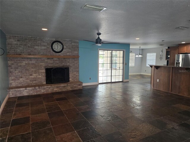 unfurnished living room with ceiling fan, a fireplace, a textured ceiling, visible vents, and baseboards