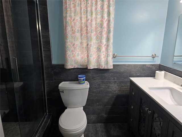 bathroom with a shower stall, vanity, tile walls, and toilet