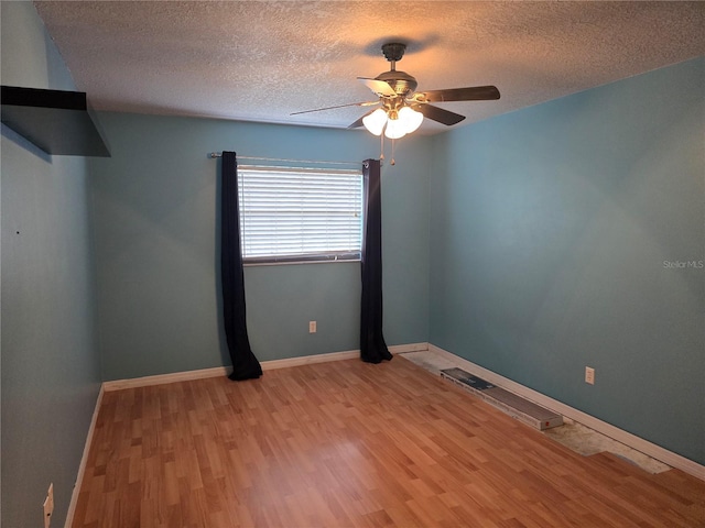 spare room featuring ceiling fan, light wood finished floors, baseboards, and a textured ceiling