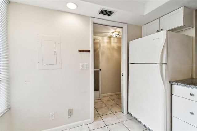 kitchen with electric panel, white cabinetry, freestanding refrigerator, light tile patterned flooring, and visible vents