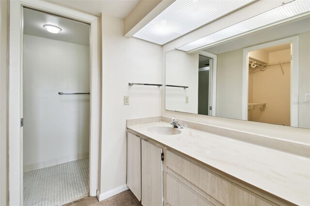 full bathroom with a spacious closet, vanity, and baseboards
