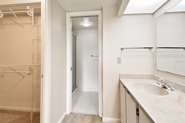 bathroom with a walk in closet, baseboards, a shower stall, and vanity